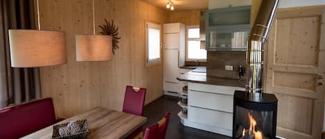 A cozy cabin interior with a dining area, a kitchen with a stove, and a large window.