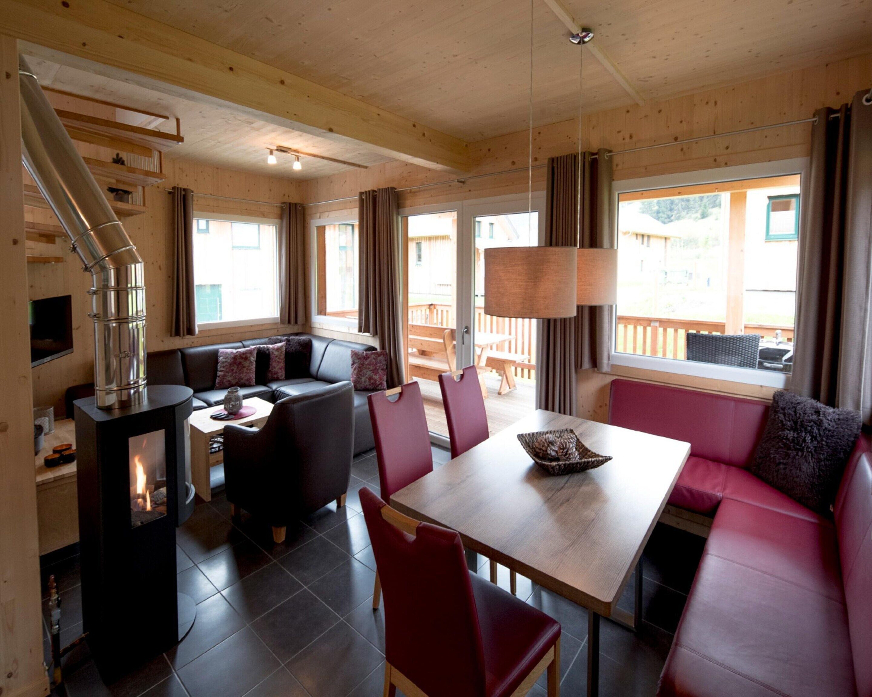 Een gezellig interieur van een blokhut met een open haard, houten wanden, een eethoek en een zithoek met uitzicht.