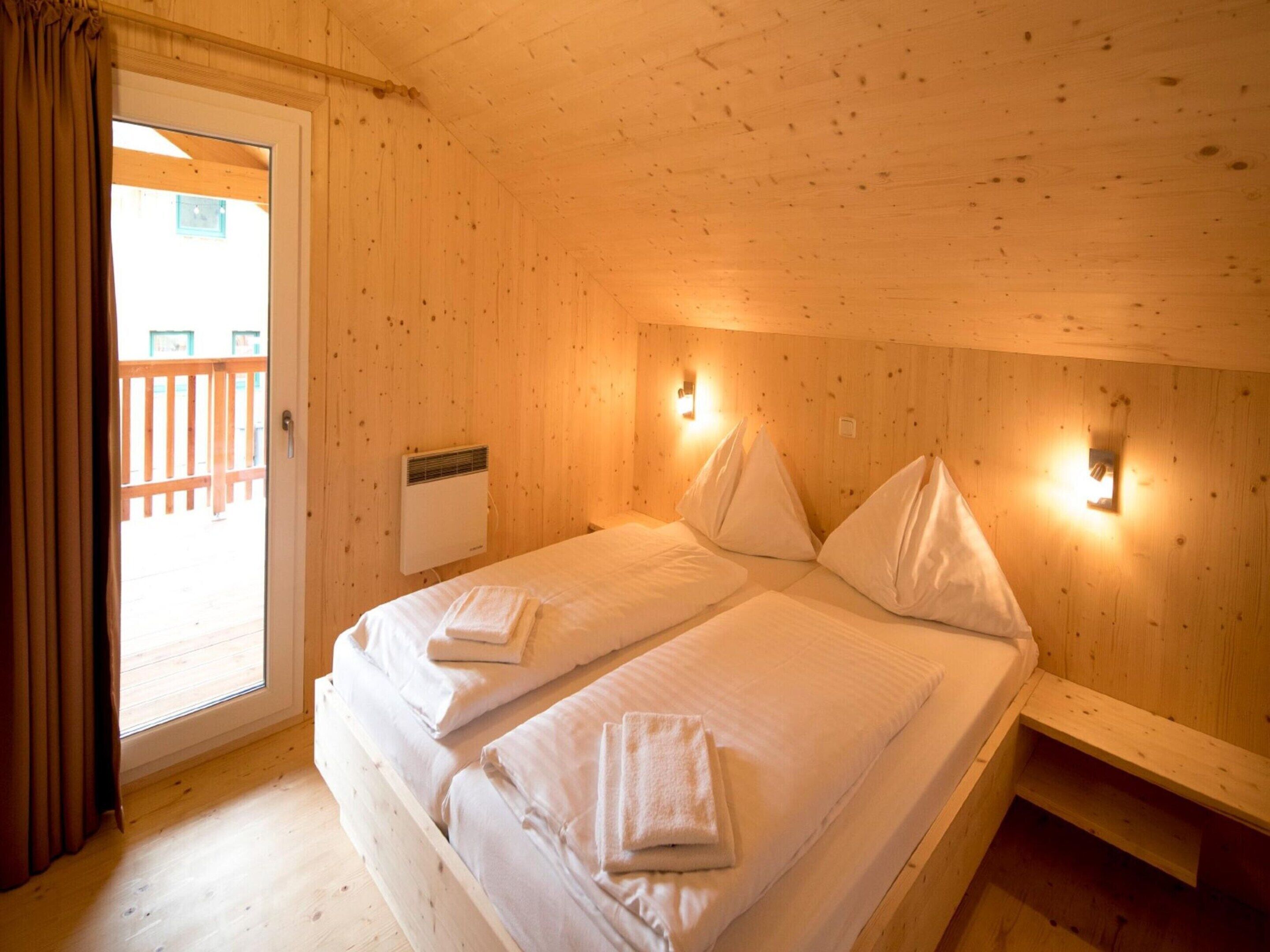 Ein Zimmer in einer Holzhütte mit zwei Betten, einer Schiebeglastür zum Balkon und einem Wandheizkörper.