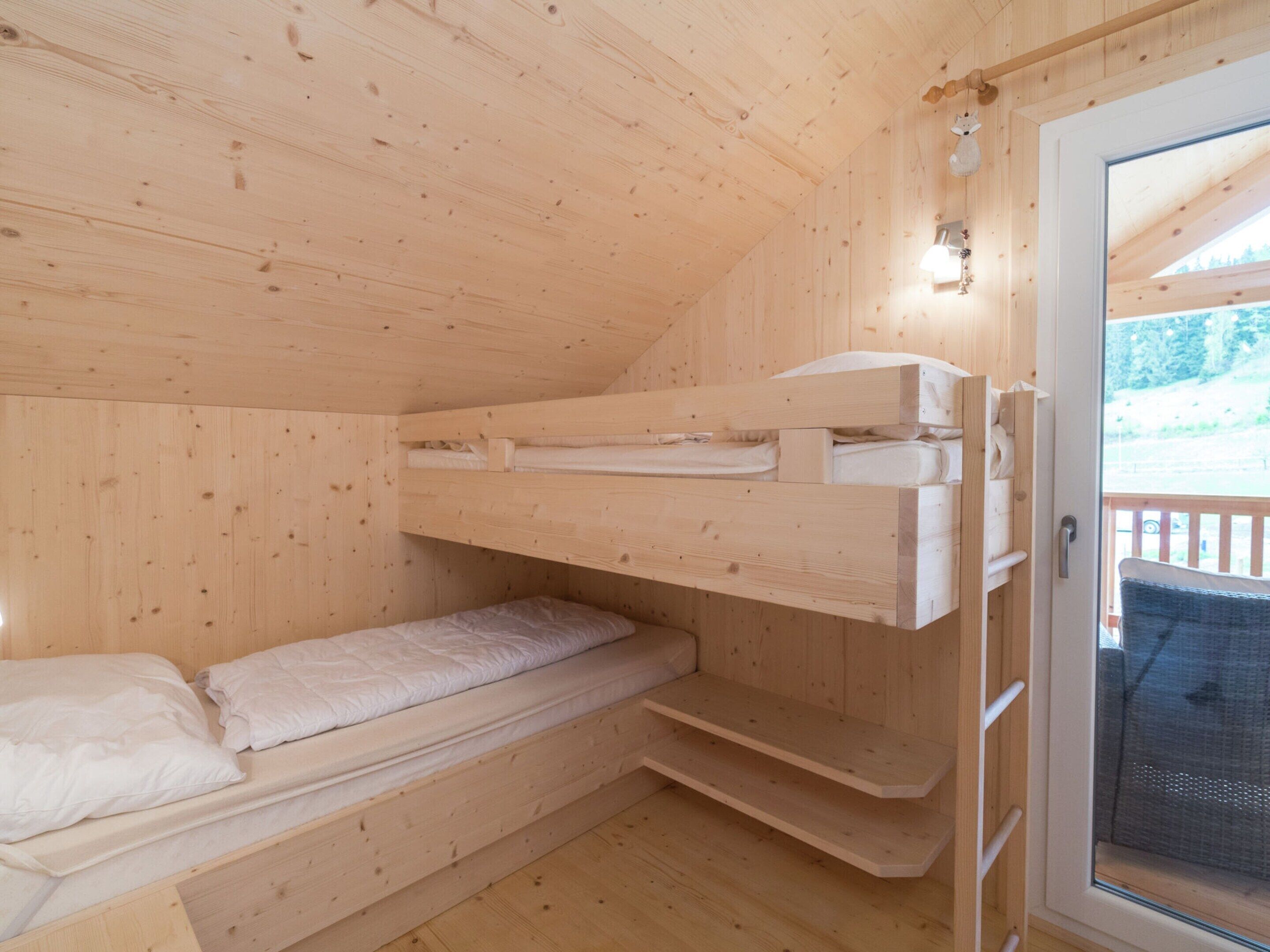 Una habitación de cabaña de madera con literas, un ventanal pequeño y una puerta.