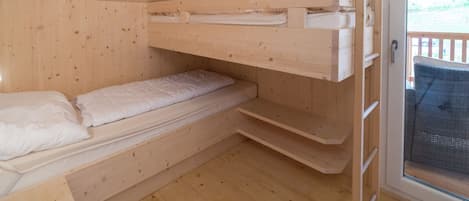Una camera in una casetta di legno con letti a castello, una piccola finestra e una porta.