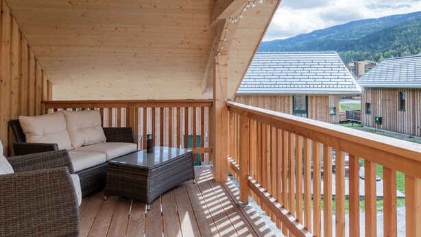 A wooden deck with wicker furniture, a glass-top table, and a view of neighboring buildings and mountains. - Attractive Chalet on the Slopes (Sankt Georgen am Kreischberg)