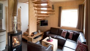 A cozy living room with a wood-burning stove, a sofa, a TV, and a staircase. - Attractive Chalet on the Slopes (Sankt Georgen am Kreischberg)