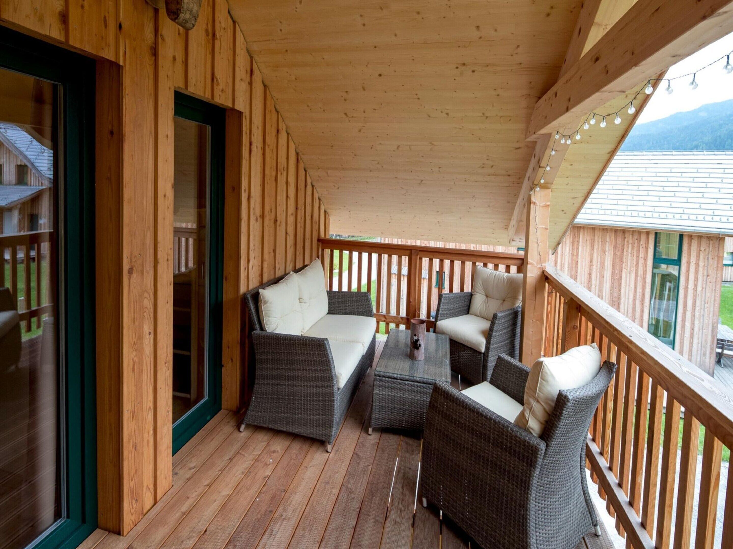 A wooden deck with wicker furniture, including a sofa and chairs, and a glass door leading to an outdoor area.