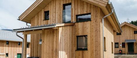 A wooden cabin with a sloped roof, a satellite dish, and a small porch with steps leading to the entrance.