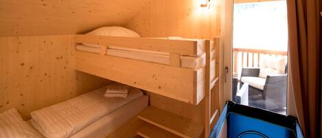 Una habitación tipo cabaña de madera con literas, una mesita y vistas a una terraza exterior.