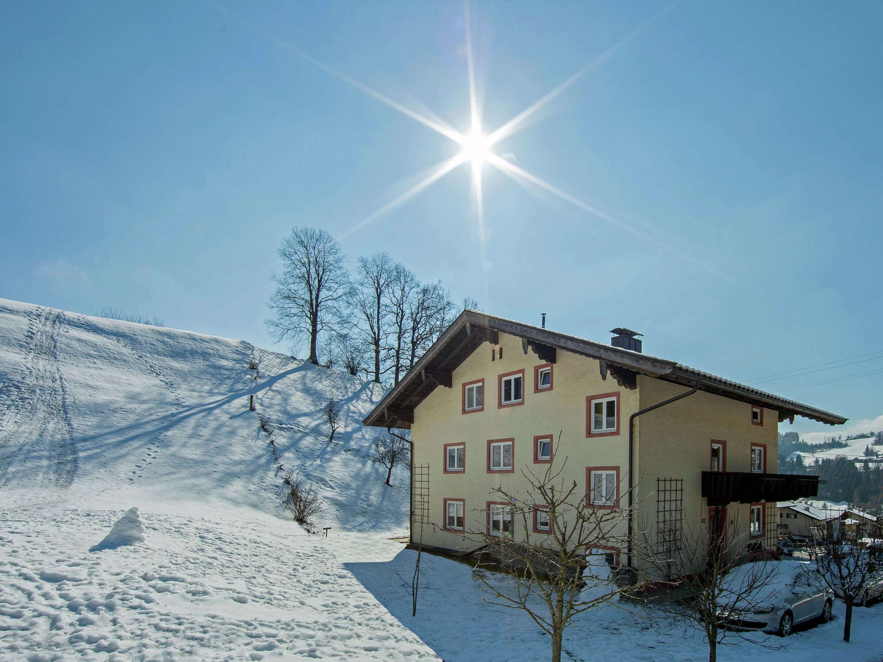 A snow-covered building with multiple windows and a sloped roof, surrounded by a snowy landscape and trees.