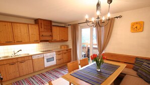 A kitchen with wooden cabinets, a sink, a dishwasher, and an oven. There is a dining table with chairs and a vase of flowers. - Huge Holiday Home in Hopfgarten im Brixental near Ski Lift (Hopfgarten im Brixental)
