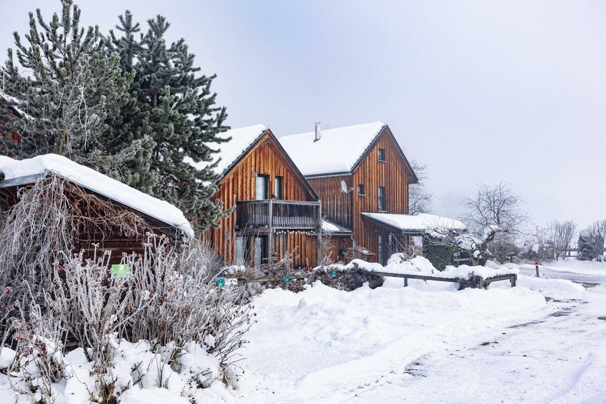 Eine Holzhütte mit einem Balkon, umgeben von schneebedecktem Boden und Bäumen.