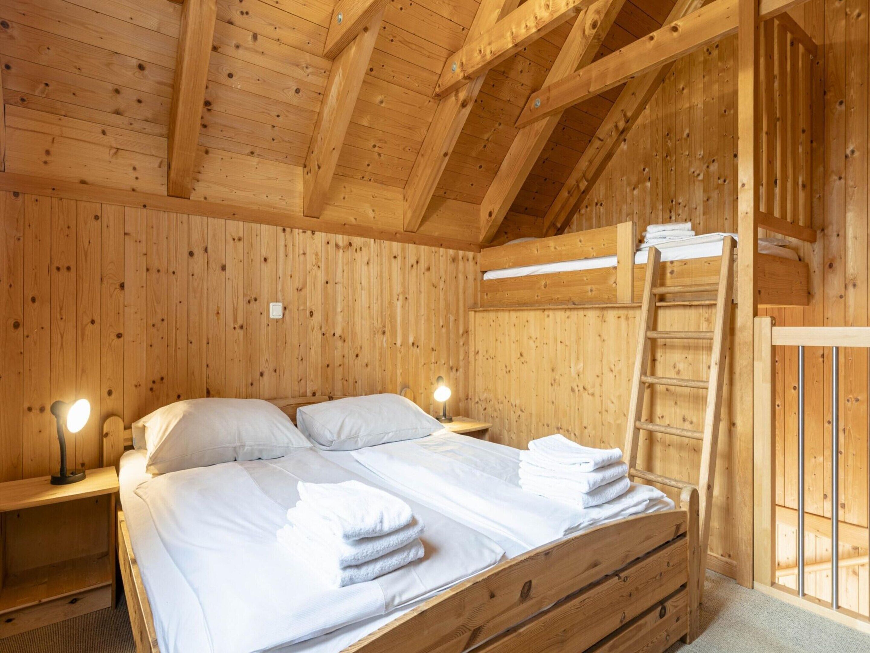 Ein Holzhütten-Zimmer mit einem Bett, zwei Nachttischen, einer Leiter und einem kleinen Fenster.