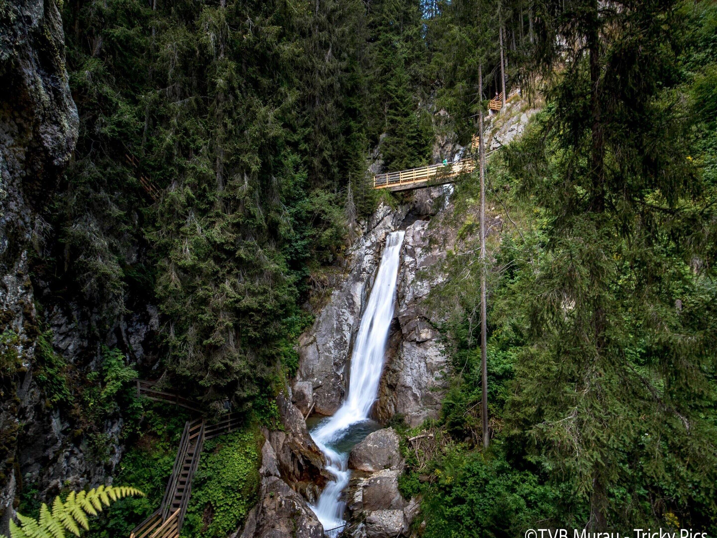 A waterfall in a forested area with a wooden walkway leading up to a viewing platform.