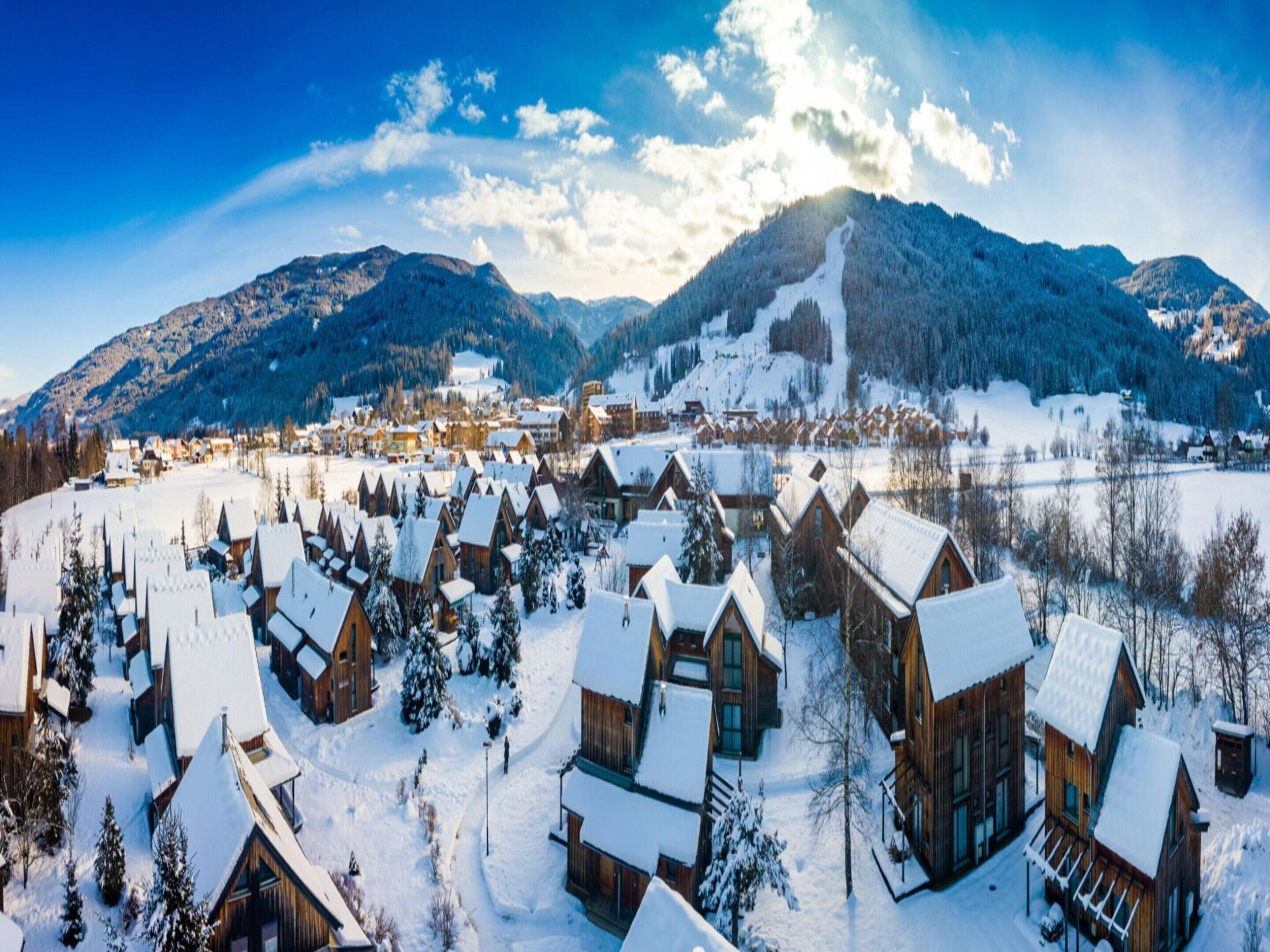 Een besneeuwd dorp met houten hutten en een berg op de achtergrond.