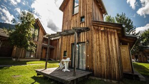 A wooden cabin with a sloped roof, a porch with chairs, and a small table. - Splendid Holiday Home in Kreischberg Murau near Ski Resort (Sankt Georgen am Kreischberg)
