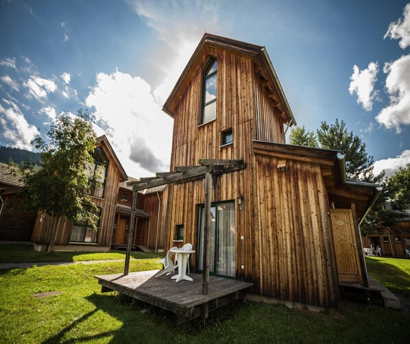 A wooden cabin with a sloped roof, a porch with chairs, and a small table. - Splendid Holiday Home in Kreischberg Murau near Ski Resort (Sankt Georgen am Kreischberg)
