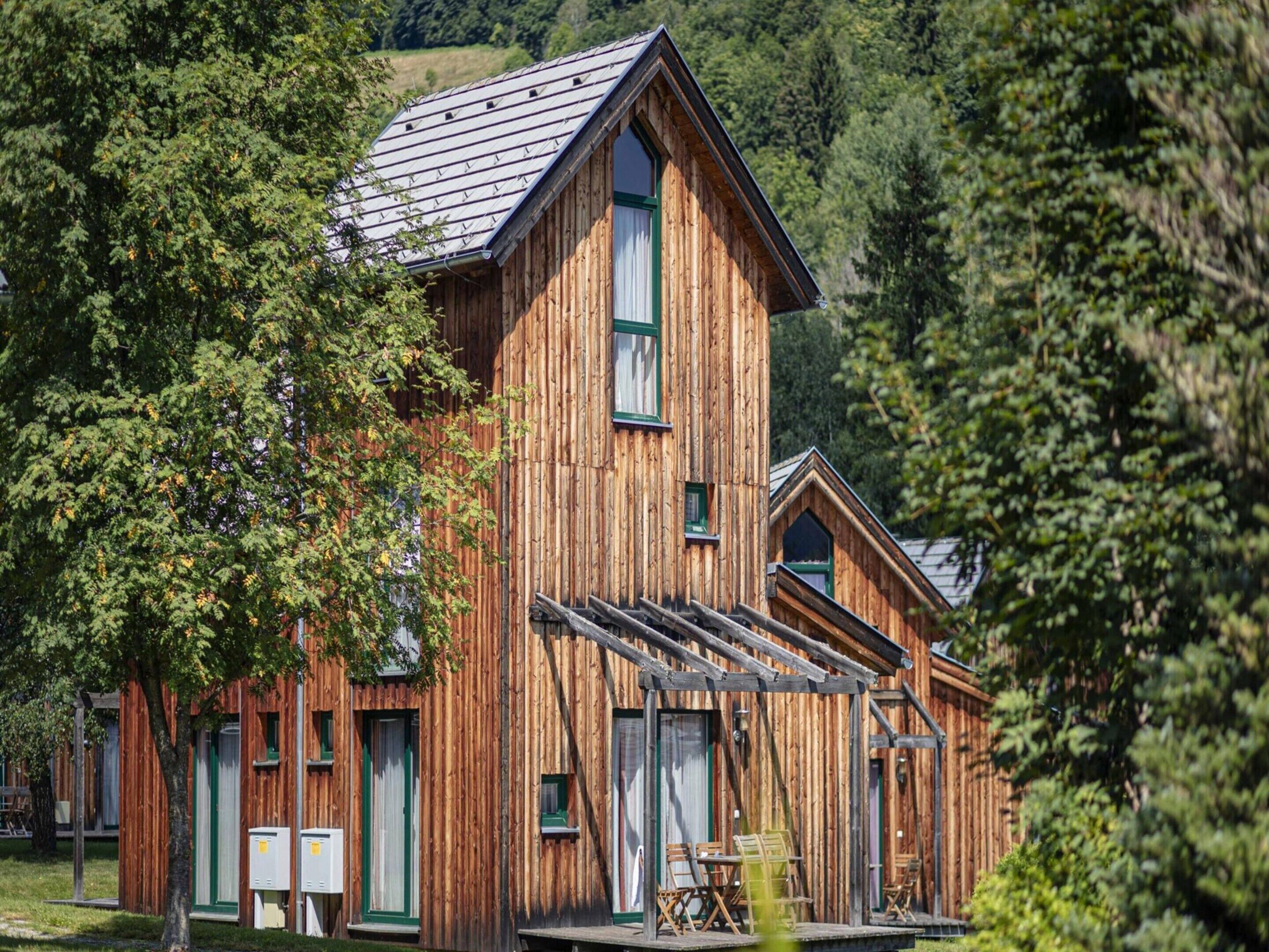 A rustic wooden cabin with a steep gabled roof, large windows, and a porch area.