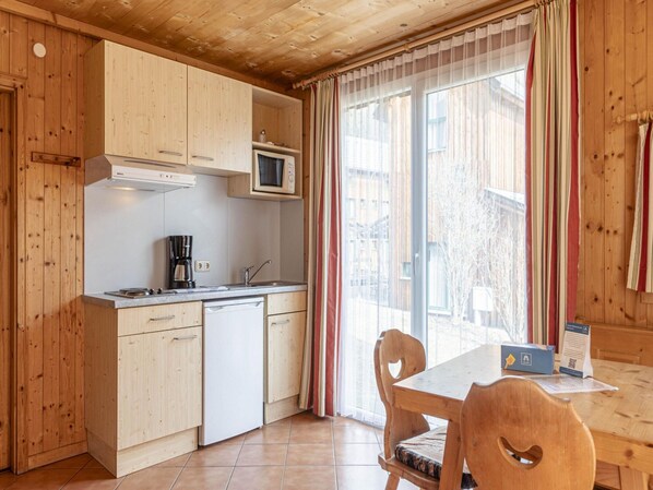 Ett kompakt kök med träskåp, en mikrovågsugn, en kaffebryggare och ett matbord med stolar.