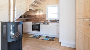 A compact kitchen with a wood-burning stove, white cabinets, and a window. - Snug Chalet With Sauna (Sankt Georgen am Kreischberg)