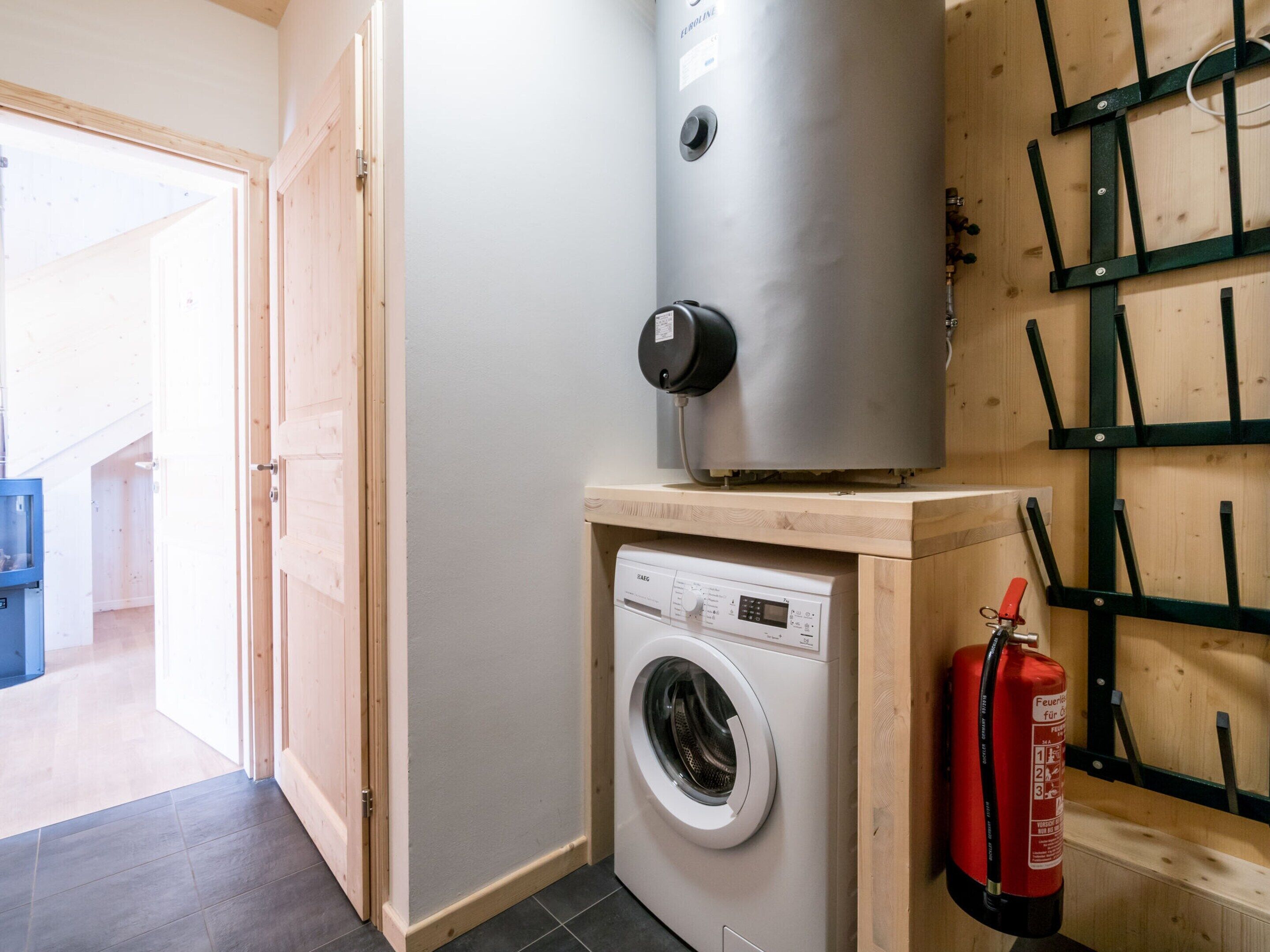 A compact laundry room with a washing machine, a water heater, and a fire extinguisher.