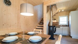 A wooden interior with a dining table set for four, a clock on the wall, and a kitchen area with a stove and cabinets. - Snug Chalet With Sauna (Sankt Georgen am Kreischberg)