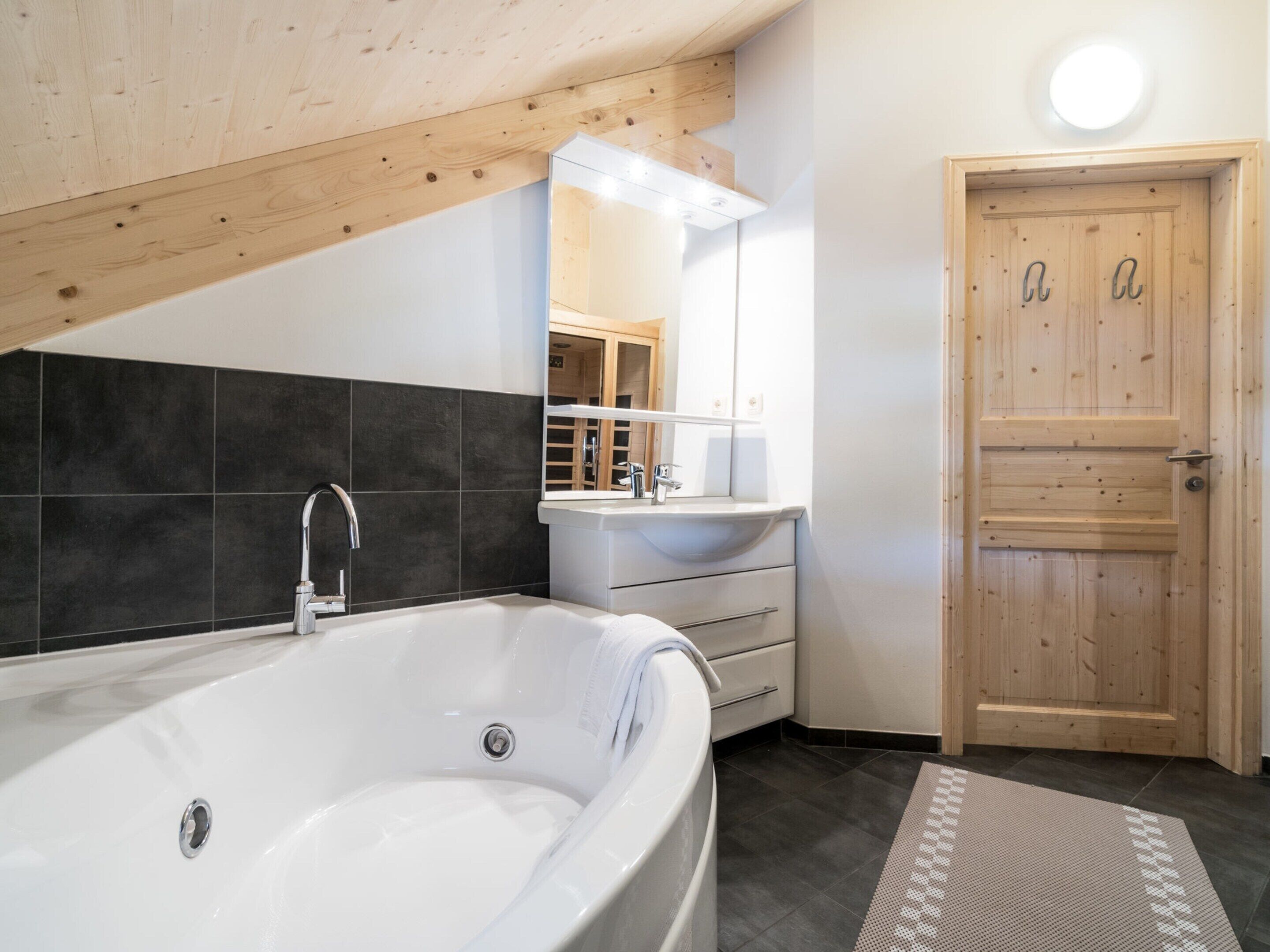 Un baño moderno con una bañera independiente, una puerta de madera y un espejo sobre el lavamanos.