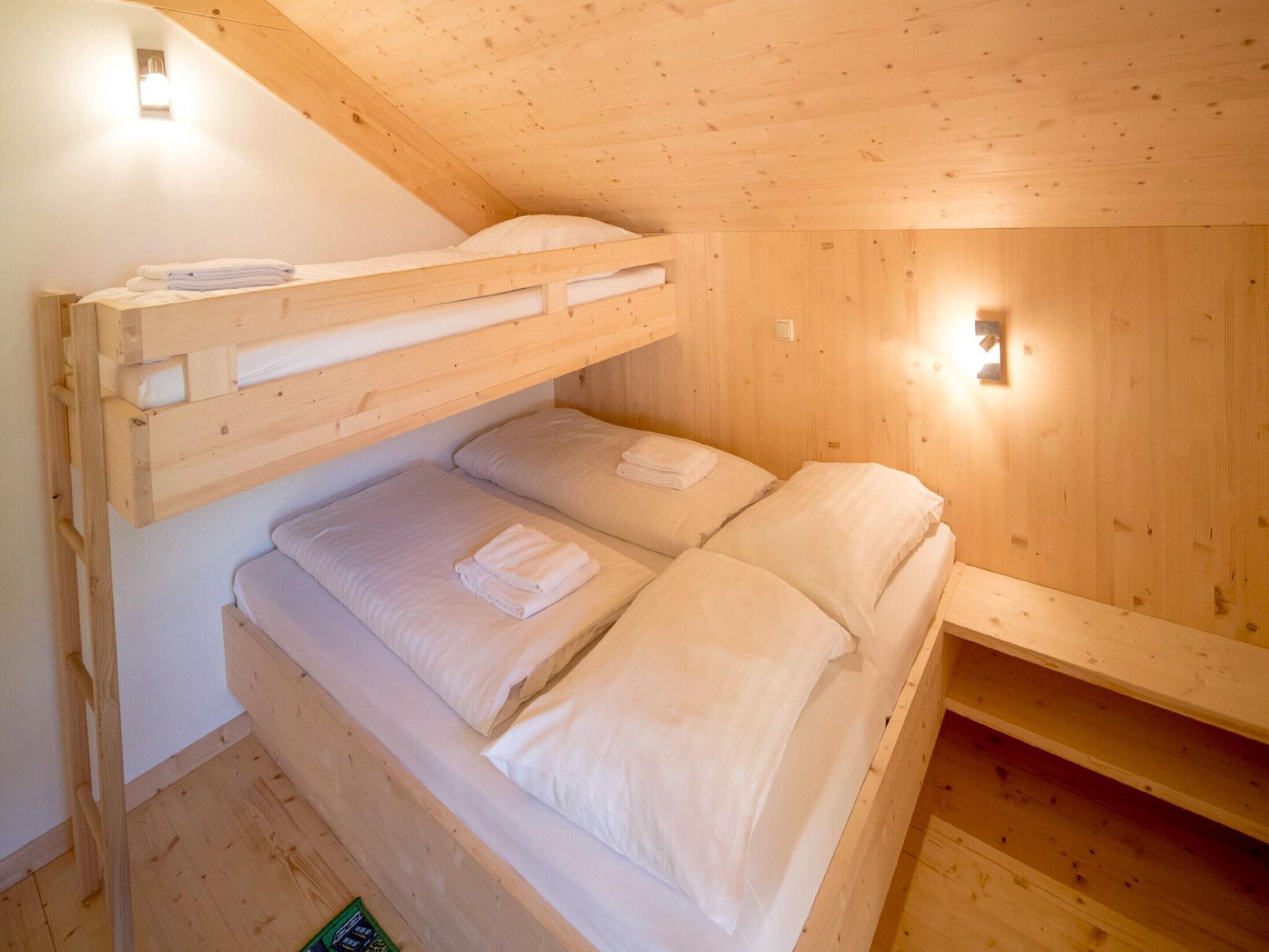 Quarto com beliche de madeira, com duas camas, cada uma com almofadas e toalhas dobradas. Há duas luminárias fixadas na parede.