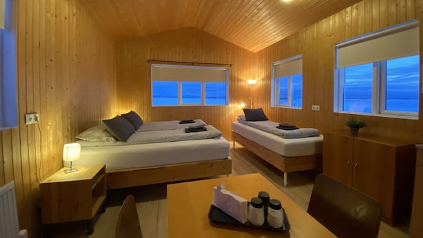 A cozy wooden cabin room with two beds, a table with salt and pepper shakers, and windows offering a view of the outdoors. - Beindalsholt (Rangárþing ytra)
