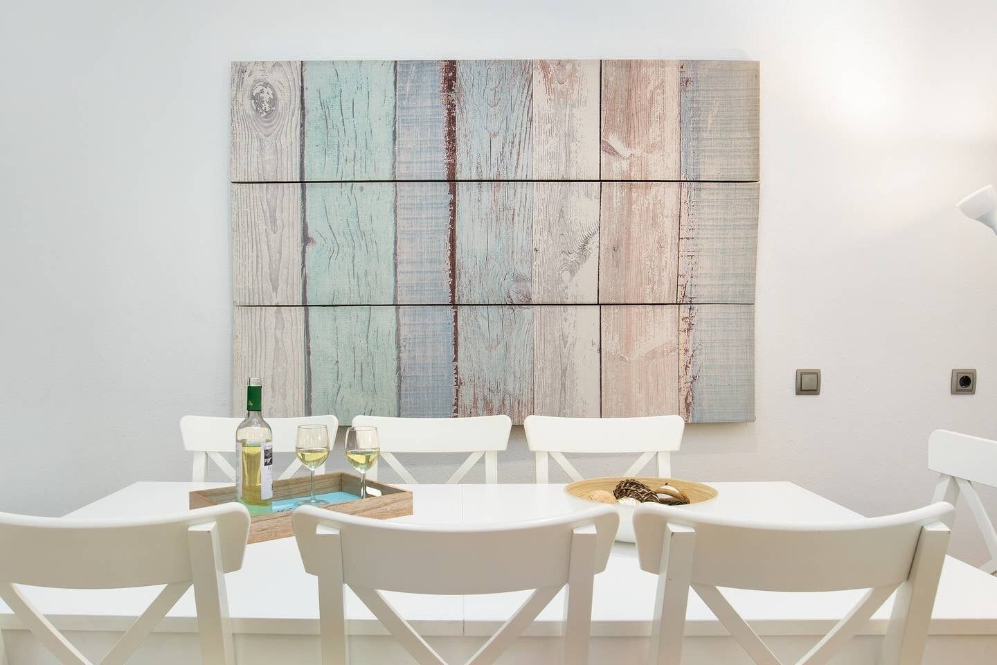 Uma sala de jantar com uma mesa branca, cadeiras brancas e um grande quadro abstrato na parede.