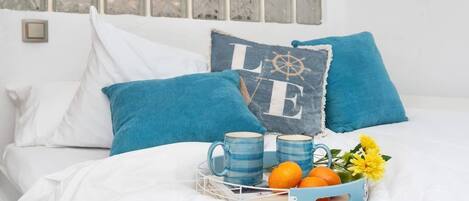 Ein Bett mit weißer Bettwäsche, blauen Kissen und einem Tablett mit zwei Tassen und Orangen.