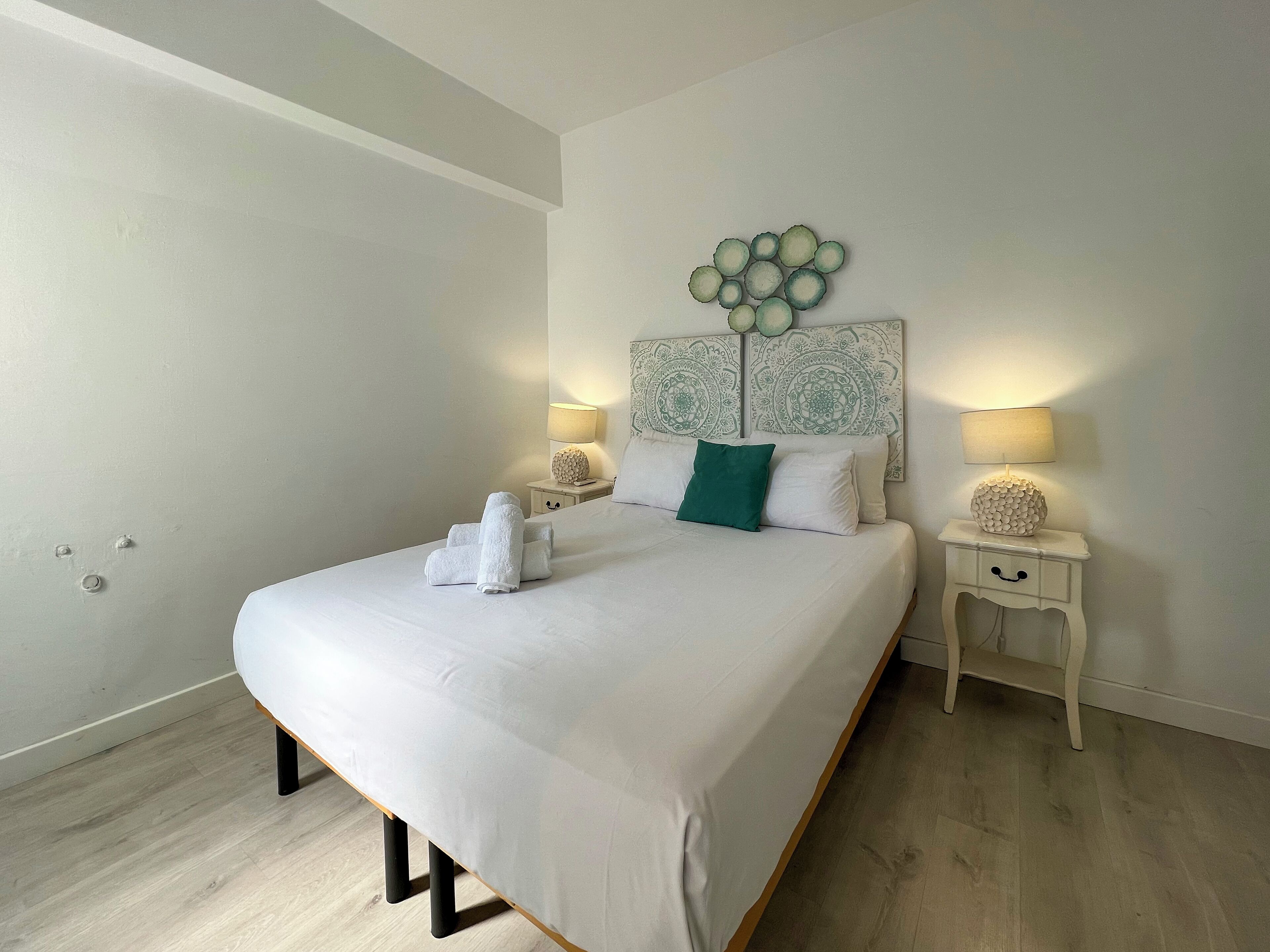 A neatly made bed with white linens, two bedside tables with lamps, and a decorative wall piece above the bed.