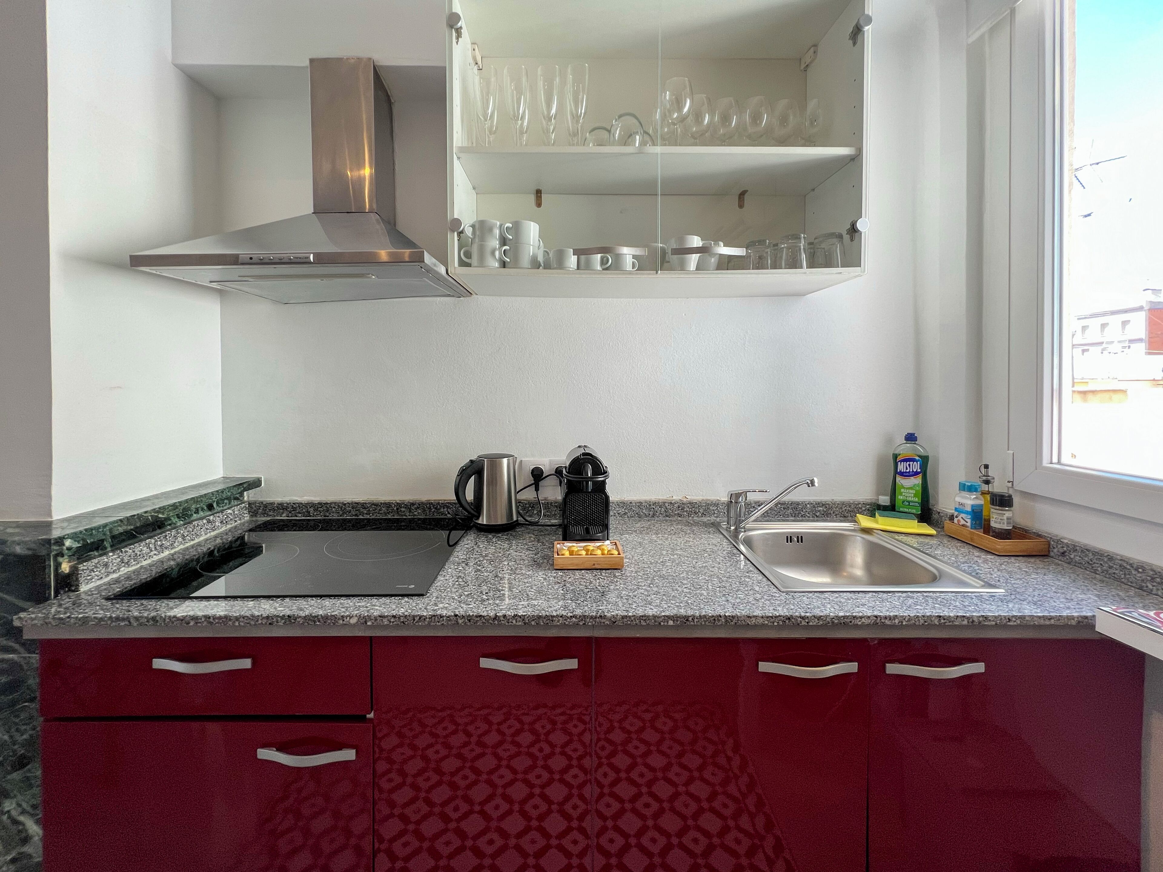 A kitchen with a stainless steel range hood, a sink, and a window with a view of buildings outside.