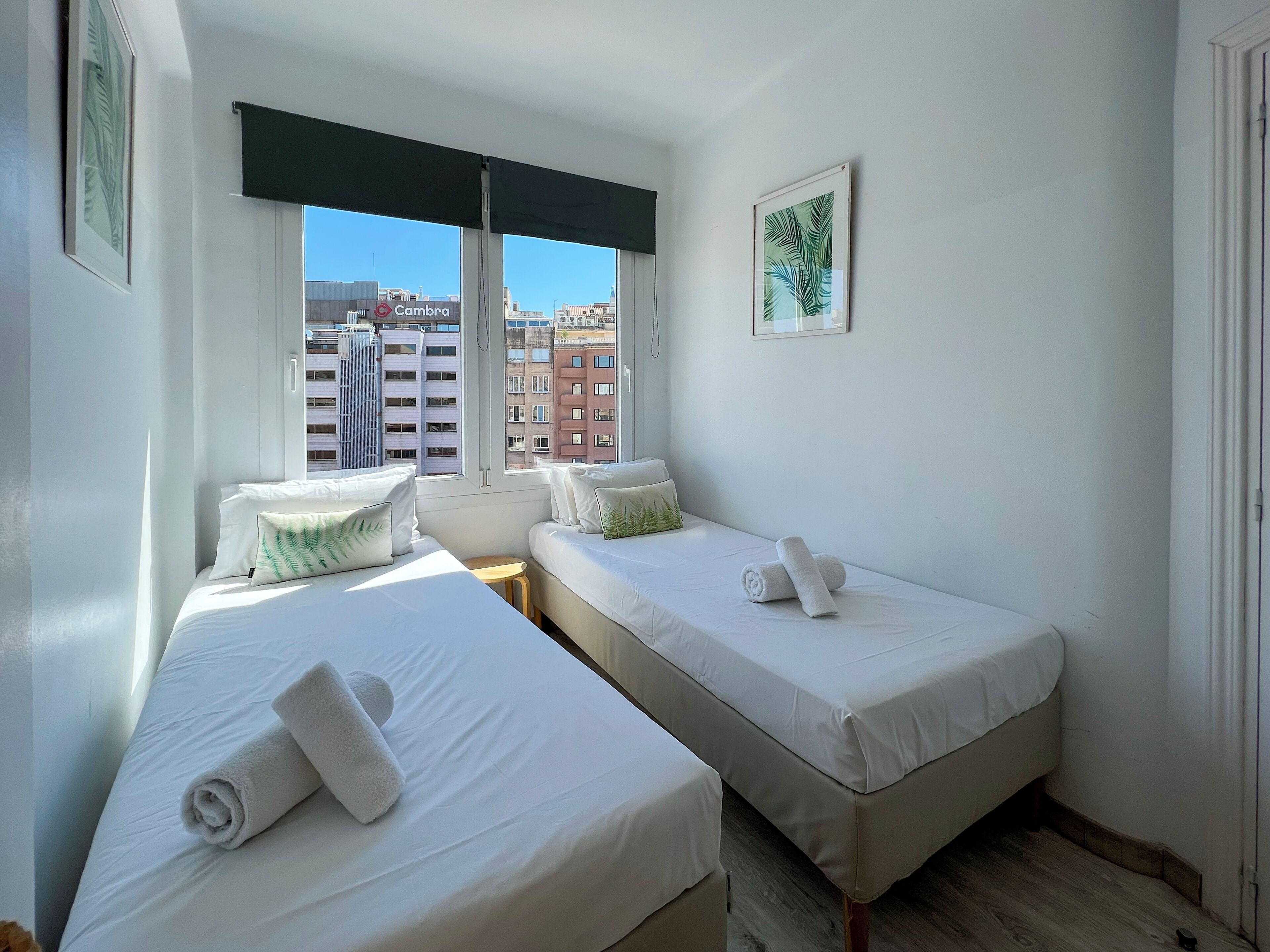 Ein Hotelzimmer mit zwei Betten, einem Fenster mit Blick auf Gebäude und einem gerahmten Bild an der Wand.
