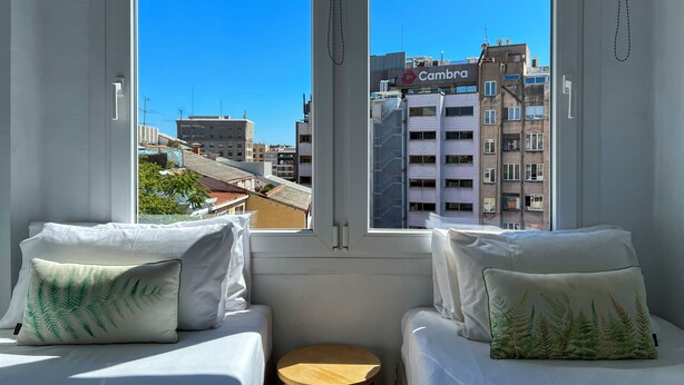 A hotel room with two beds, a small wooden stool, and a view of the cityscape through large windows. - Stay U-nique Apartment Sèneca (Barcelona)