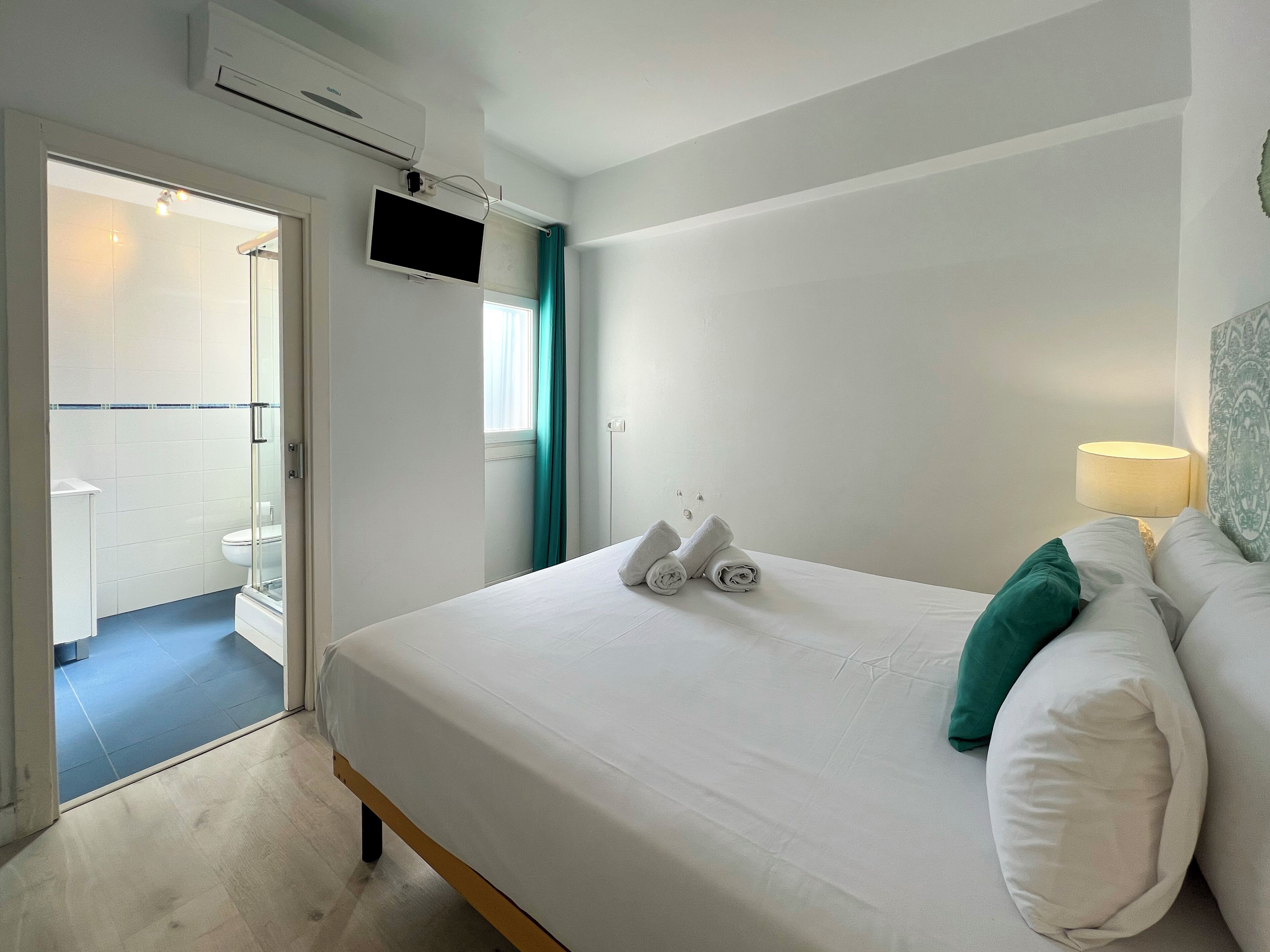 A hotel room with a bed, a TV mounted on the wall, and a bathroom visible through an open door.
