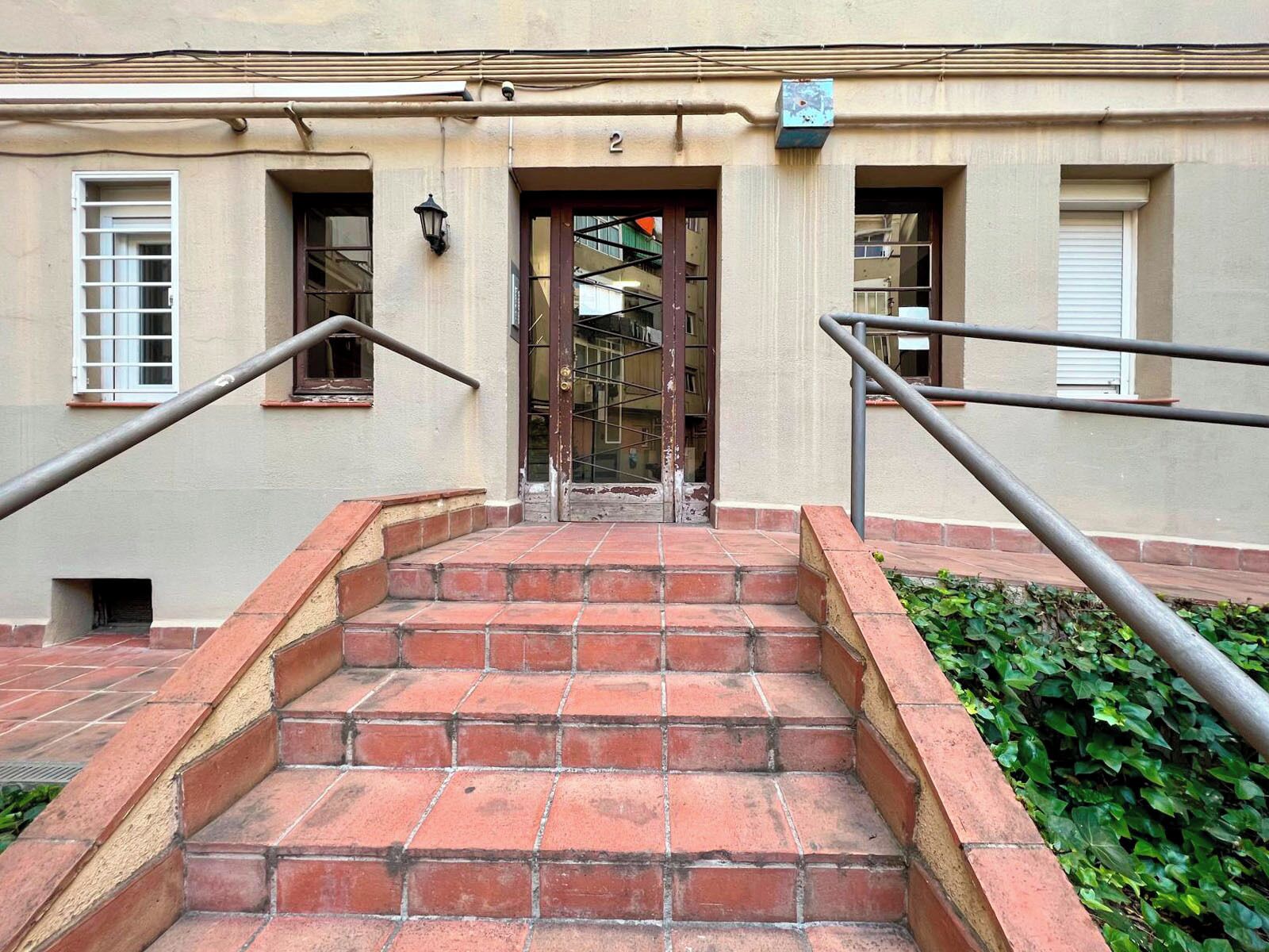 A set of red brick stairs leading to a building entrance with a metal railing on each side.