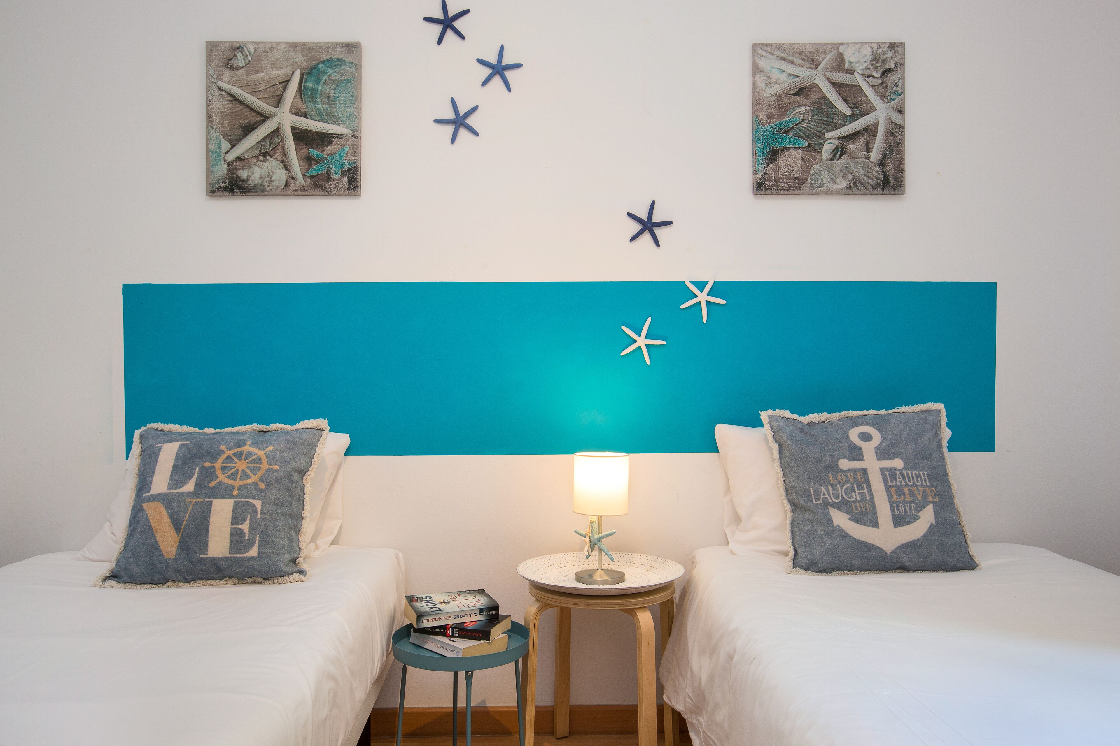 Une chambre avec deux lits, une table de chevet avec une lampe et des décorations murales représentant des étoiles de mer.