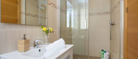 A modern bathroom with a glass shower enclosure, a wooden vanity with a white sink, and a mirror above the vanity.