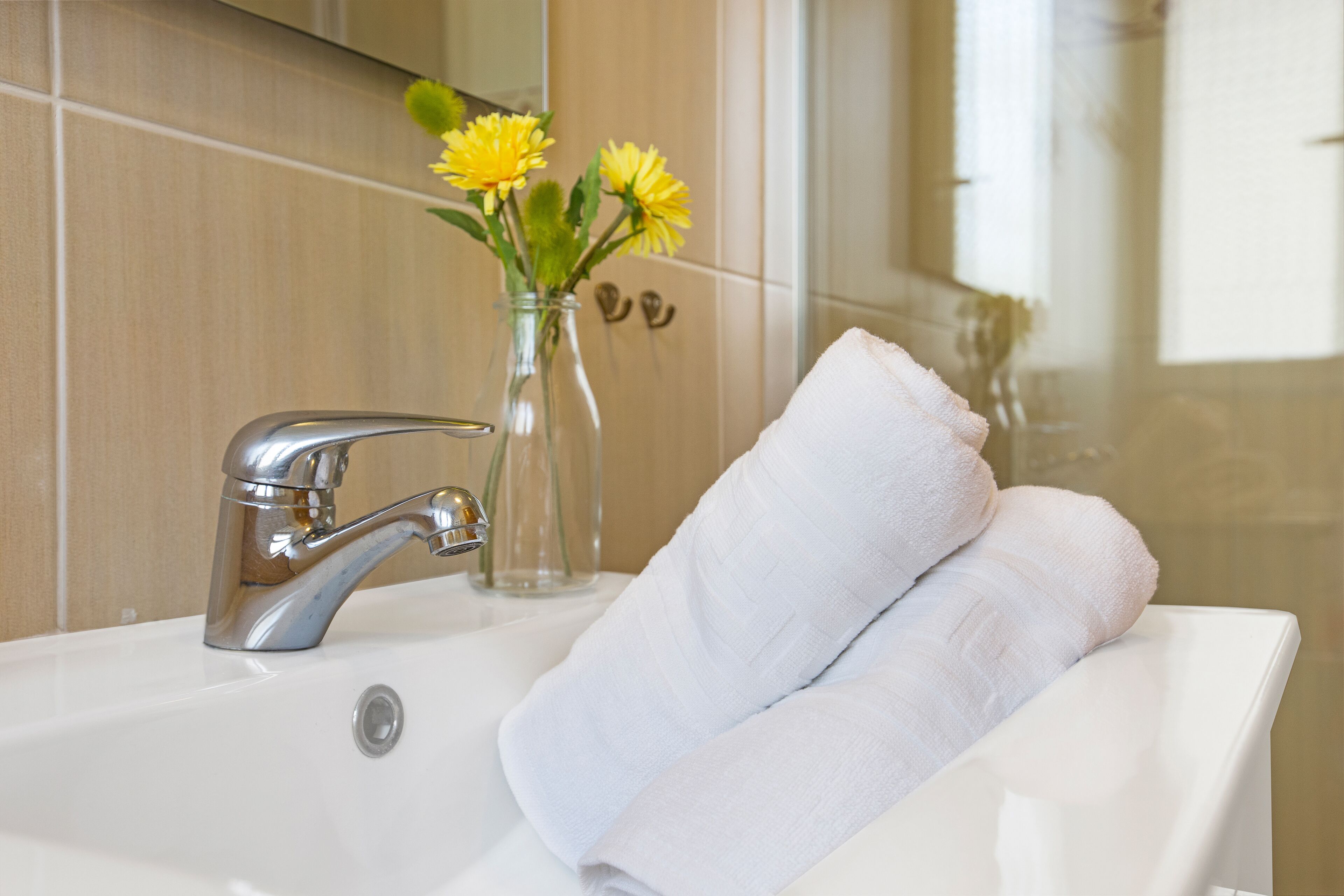 Un baño con lavamanos blanco, grifo plateado y un jarrón con flores amarillas.