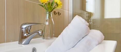 Un baño con lavamanos blanco, grifo plateado y un jarrón con flores amarillas.