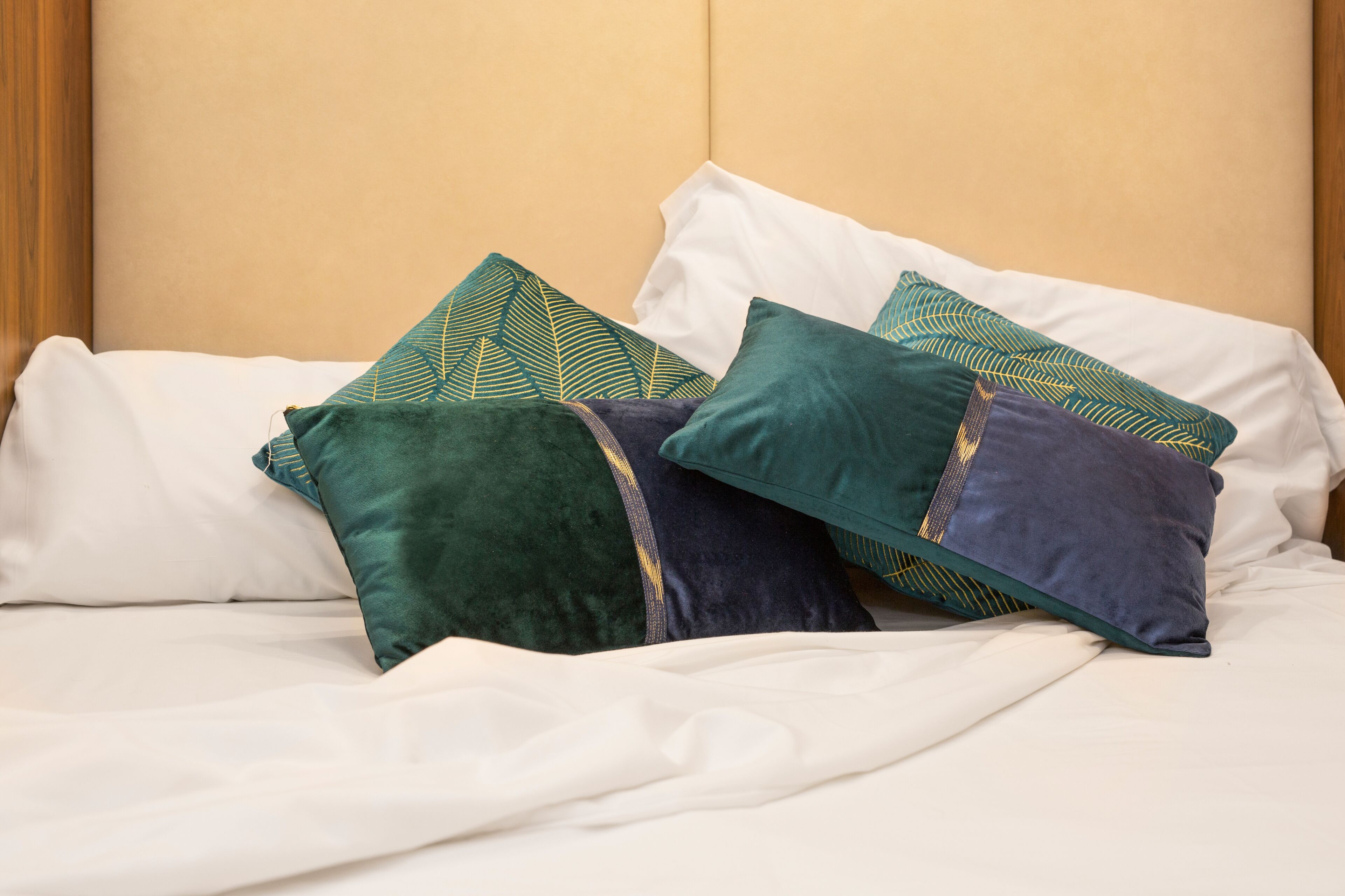 A neatly made bed with white sheets and three decorative pillows in green, blue, and white.