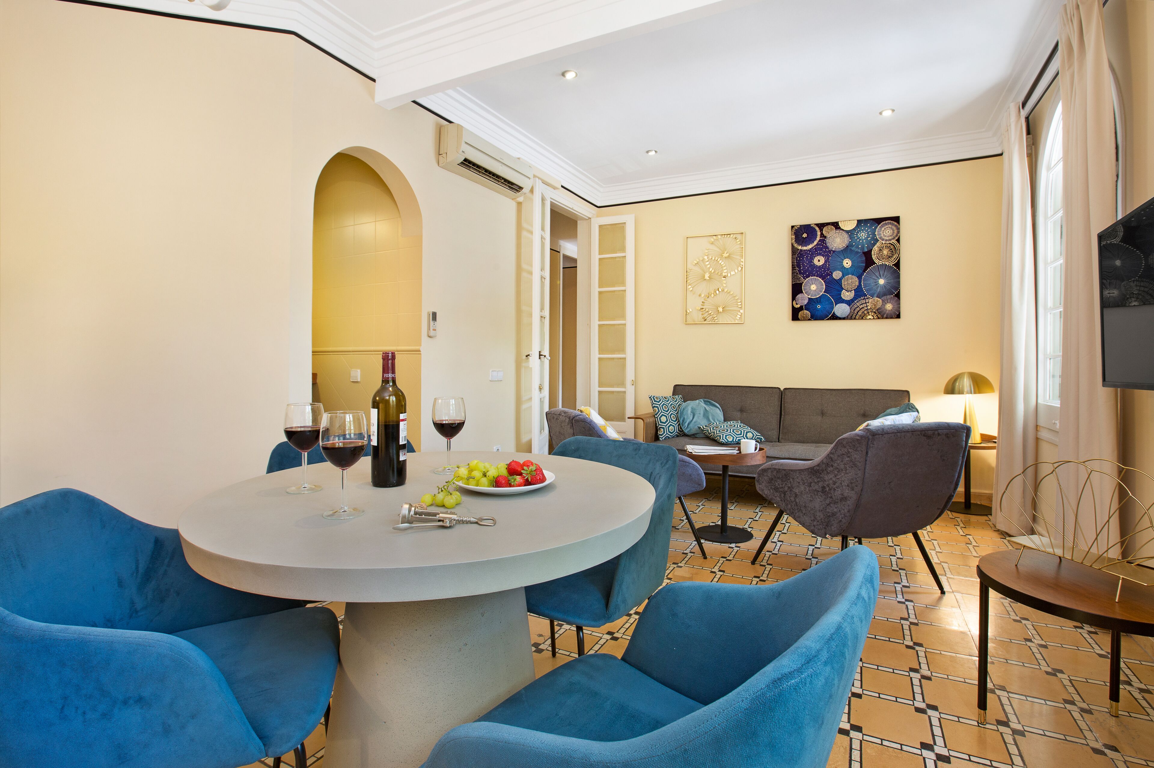 Un coin repas avec une table ronde, des chaises recouvertes d’un tissu bleu et une assiette de fruits.