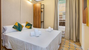 Una camera d'albergo con un letto, asciugamani, un armadio in legno, una finestra con tende e un pavimento piastrellato.