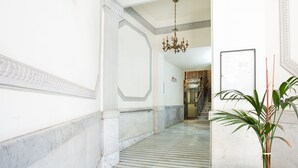 Un corridoio in marmo con un lampadario, una scala e una pianta in vaso.