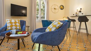 Un soggiorno moderno con due poltrone blu, un tavolino da caffè con un giornale e della frutta, una televisione a schermo piatto e un'area pranzo con uno sgabello da bar.