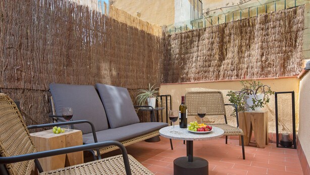 Patio esterno con mobili in vimini, un tavolo rotondo con una bottiglia e bicchieri, e una pianta in vaso.
