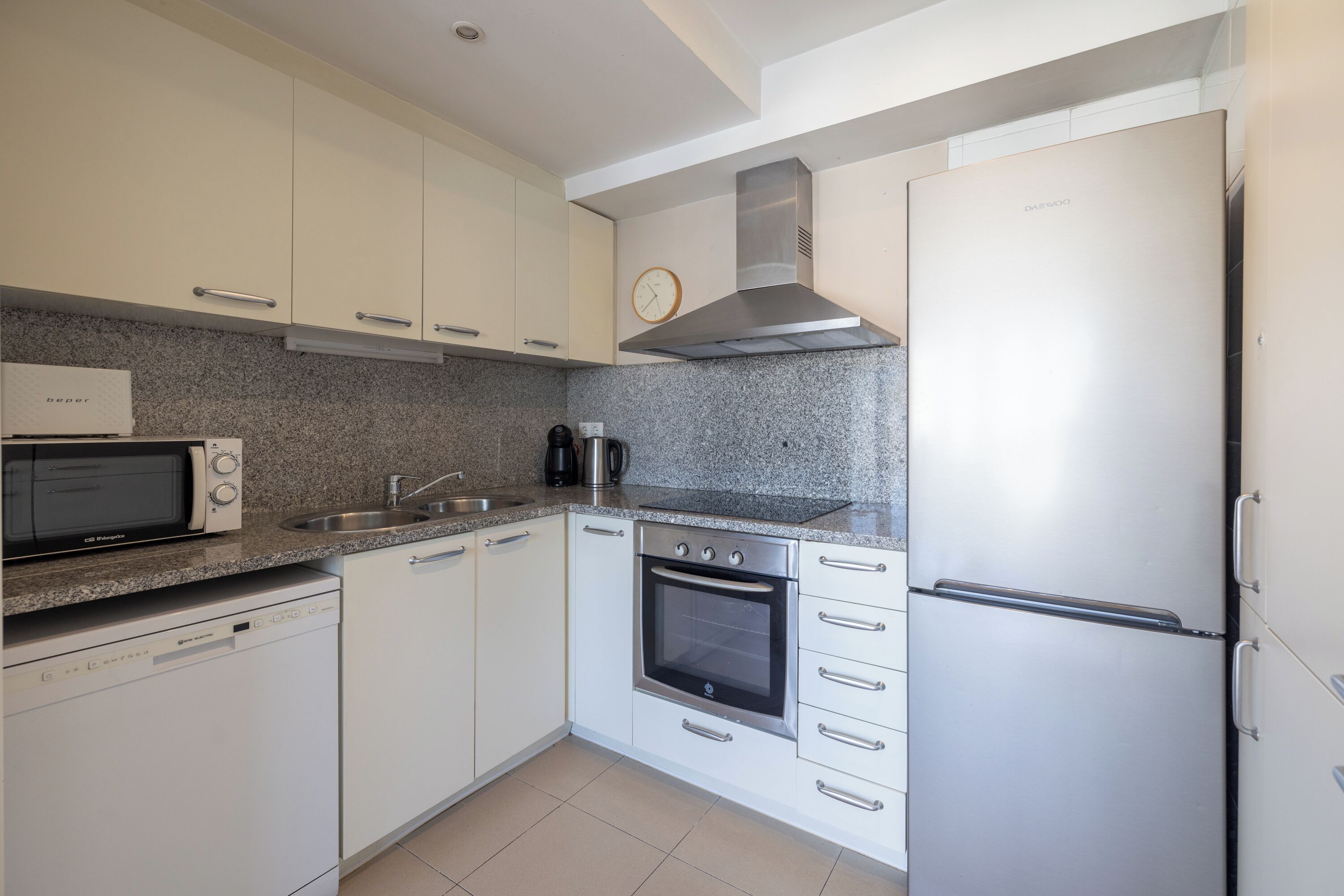 A kitchen with white cabinets, a stainless steel range hood, a microwave, a coffee maker, and a refrigerator.