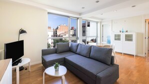 Una sala de estar moderna con un sofá seccional, un televisor de pantalla plana, una mesita con una planta y vistas de la ciudad a través de amplios ventanales.
