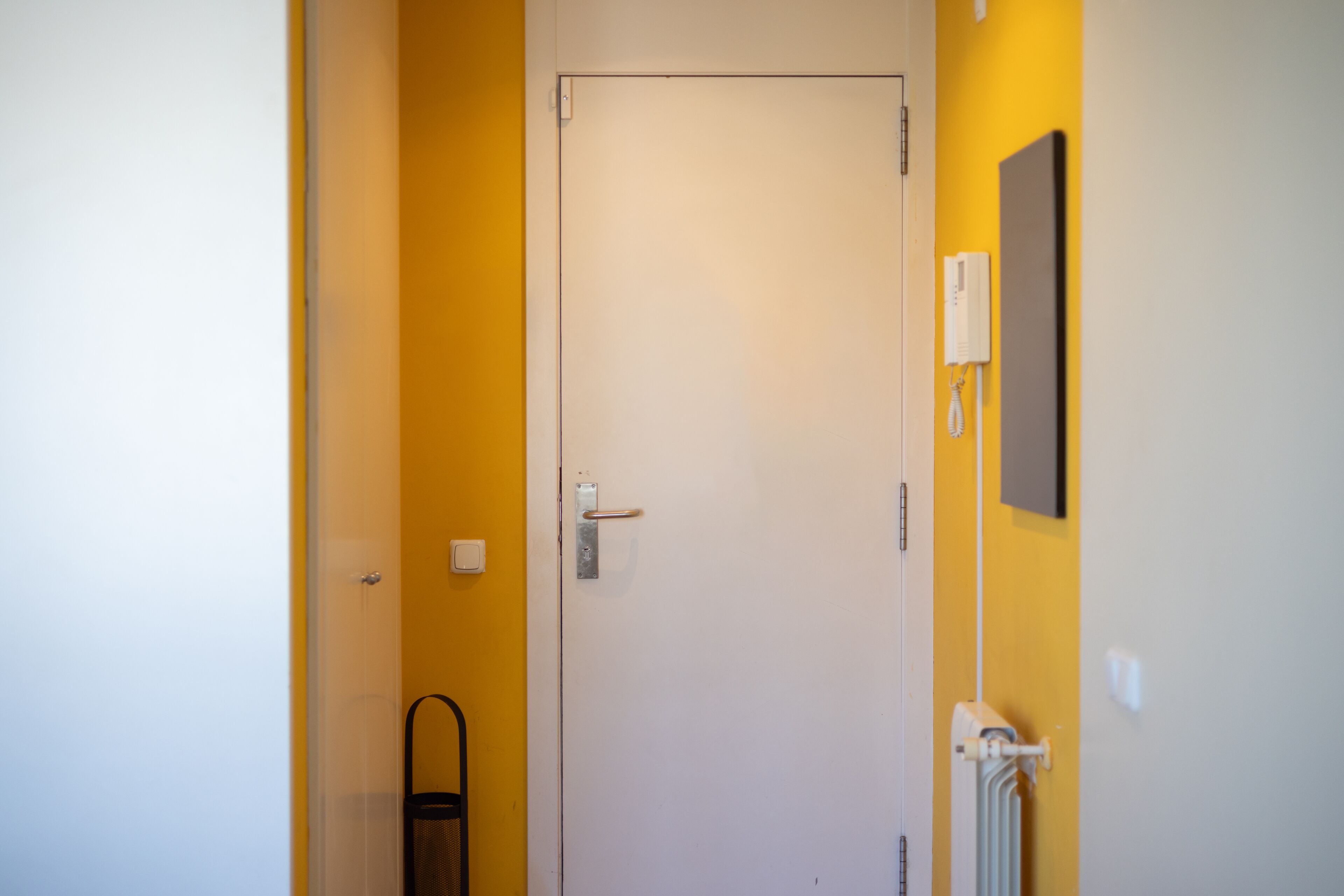 Eine Tür mit Griff, ein Heizkörper und ein Lichtschalter an der Wand.