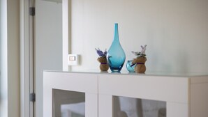Un mueble blanco con puertas de cristal, un florero azul y pequeñas macetas en la parte superior.