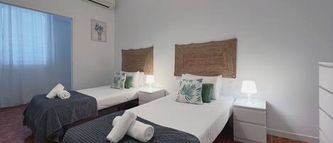 Habitación de hotel con dos camas, cada una con cabecera, mesitas de noche con lámparas, una ventana con cortinas y un equipo de aire acondicionado en la pared.