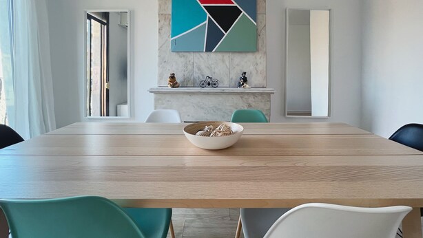 A modern meeting room with a wooden table, teal and white chairs, a marble wall with a geometric painting, and a small shelf with figurines. - Stay U-nique Apartments Casanova (Barcelona)